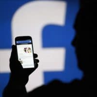 A man is silhouetted against a video screen with an Facebook logo as he poses with an Samsung S4 smartphone in this photo illustration taken in the central Bosnian town of Zenica, August 14, 2013. REUTERS/Dado Ruvic/File Photo.