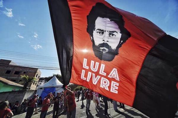 | In this July 8 2018 file photo a supporter of former Brazilian President Luiz Inacio Lula da Silva waves a banner decorated with an image depicting da Silva and message that reads in Portuguese Free Lula in front of the Federal Police Department where he is serving jail time in Curitiba Brazil | Photo Credit AP | MR Online