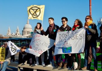 The author, Dr. Claire Wordley (right), joins Extinction Rebellion protesters blocking Blackfriar’s Bridge. Diner Ismail waves the Extinction symbol, an hourglass inside a circle representing the planet, over St. Paul’s Cathedral in the background. Photo Credit: Jane Carpenter.