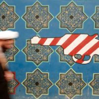 An Iranian cleric walks past a mural on the wall of the former U.S. embassy