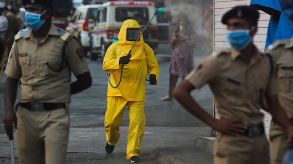 | A civic worker sanitizes an area as policemen stand guard after a protest against the extension of the lockdown at a slum in Mumbai India April 14 2020 Rafiq Maqbool | AP | MR Online