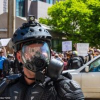 A police officer wears a gas mask at a recent protest over police brutality and racism. Credit: Becker1999 via Flickr. CC BY 2.0.