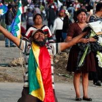 A coca leaf producer kneels holding a bible with his arms outspread asking police to open the way so a march by supports of Evo Morales may continue to Cochabamba, Bolivia, Nov. 16, 2019. Juan Karita | AP