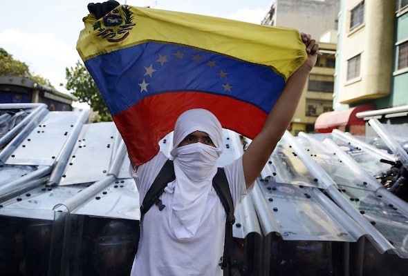 | VENEZUELAOPPOSITIONDEMO A demonstrator holds a Venezuelan flag in front of riot policemen during an opposition demo against the government of Venezuelan President Nicolas Maduro in Caracas on February 12 2014 Unidentified assailants on a motorcycle fired into a crowd of antigovernment protesters wounding at least two people AFP PHOTO JUAN BARRETO | MR Online
