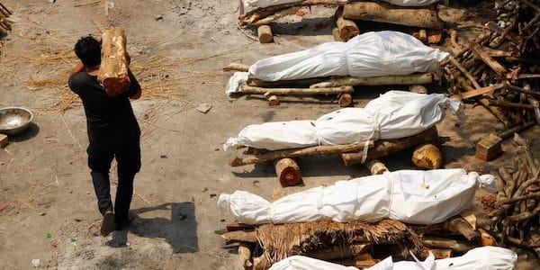| A man carrying wood walks past the funeral pyres of those who died from the coronavirus disease COVID19 during a mass cremation at a crematorium in New Delhi India April 26 2021 Photo ReutersAdnan Abidi | MR Online