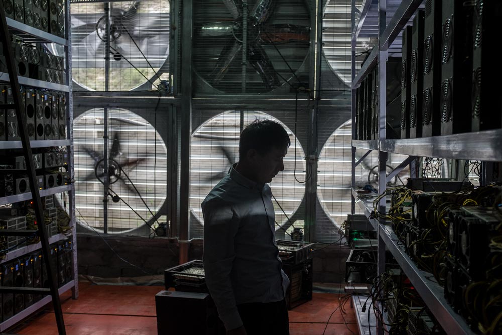 A manager stands near a wall of fans inside a bitcoin mine in rural Sichuan province, 2016. Liu Xingzhe/People Visual