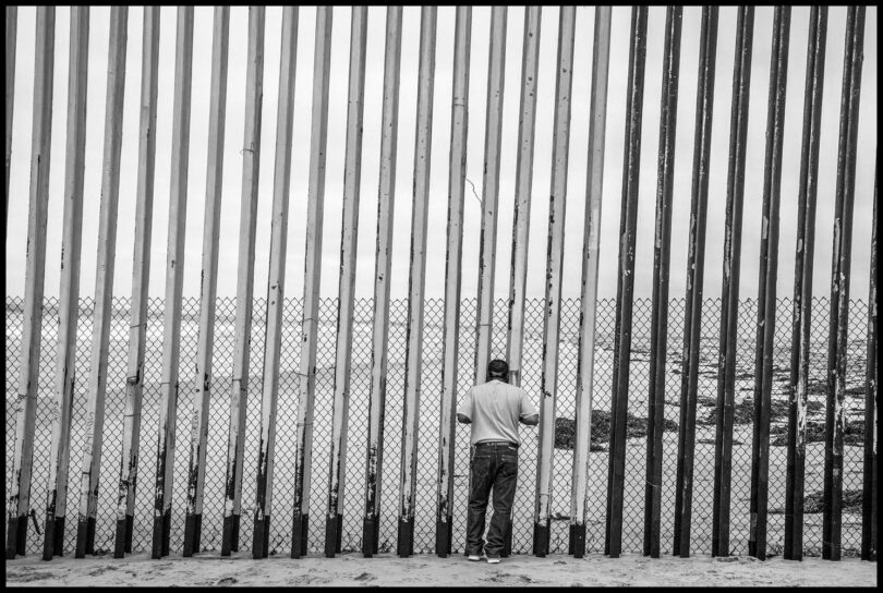 | A man on the Mexican side of the border wall between Mexico and the US looks through the bars where the wall runs into the Pacific Ocean | MR Online