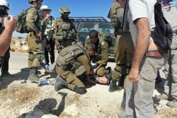 An Israeli soldier kneels on the neck of an Israeli left-wing activist during an attempt to bring water to Palestinian communities in the South Hebron Hills, April 17, 2021