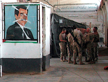 U.S. Army soldiers confer near a defaced mural of Saddam Hussein at the Baghdad Central Detention Facility, formerly Abu Ghraib Prison, in Baghdad, Iraq, Oct. 27, 2003. (U.S. National Archives)
