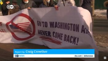 Screenshot of German public broadcaster Deutsche Welle showing protesters holding a banner that reads, “Go to Washington and never come back!”. 