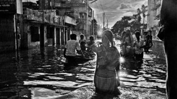 Shahidul Alam/Drik/Majority World (Bangladesh), The resilience of the average Bangladeshi is remarkable. As this woman waded through the flood waters in Kamalapur to get to work, there was a photographic studio ‘Dreamland Photographers’, which was open for business, 1988.