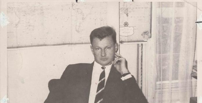 archival photo of Zbigniew Brzezinski sitting in front of a world map