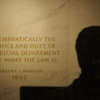 First Floor at the Statute of John Marshall in the foreground, shadowed, quotation from Marbury v. Madison (written by Marshall) engraved into the wall. United States Supreme Court Building. Image: swatgesture. Source: Wikimedia Commons