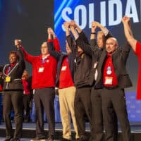 Newly-elected UAW leaders, including Secretary-Treasurer Margaret Mock (third from left) and President Shawn Fain (fourth from left) at the convention on March 29, 2023. Fain said “The rumble of the election is finished” and called on members to unite against the employers. Photo: Jim West, jimwestphoto.com.