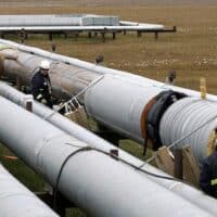 BP workers, in the background, remove insulation from an oil transit pipeline at the Prudhoe Bay oil field on Alaska's North Slope. [AP Photo/Al Grillo]