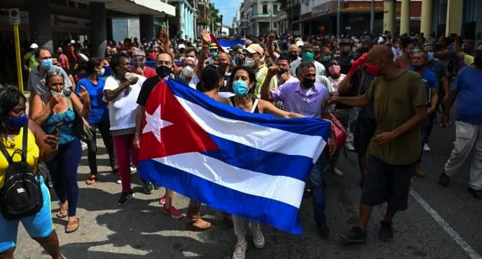 The Washington Post featured this photo as an example of anti government protests but it is clearly a pro government rally in which the demonstrators are waving the Cuban flag in solidarity with the Cuban Revolution The man behind the flag in the baseball cap is Gerardo Hernández a well known leader of the Committees for the Defense of the Revolution member of the Central Committee of the Cuban Communist Party and one of the Cuban 5 who spent 16 years in prison in the US framed for his work helping to stop terrorist attacks against the Cuban people Source washingtonpostcom