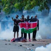 Young Kenyan protesters hold a Kenyan flag over the body of a fellow youth killed by the police during peaceful protests in Nairobi, Kenya, on 25th June 2024. Photo by Festo Lang