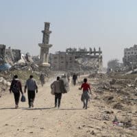 Refugees walk down a road in Gaza, surrounded by ruined buildings.