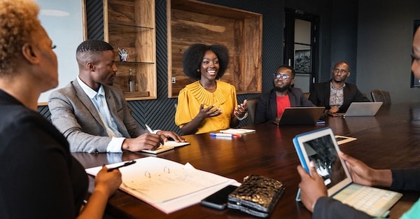 MR Online | View between colleagues with focus on African professional in early 30s looking across conference table at young associate smiling and gesturing as she speaks Photo by Johnny Greig | MR Online