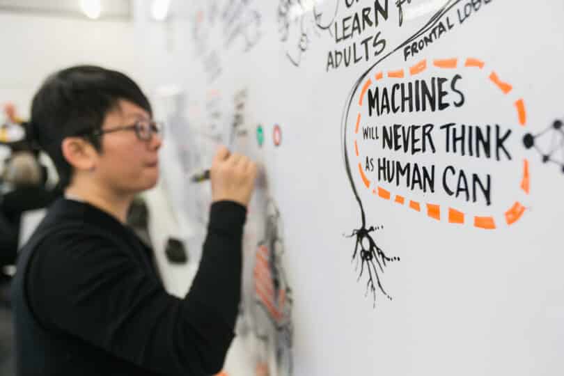  | An East Asian man writes on a white board To his right is a text bubble on the board that reads in all capitals MACHINES WILL NEVER THINK AS HUMANS CAN | MR Online