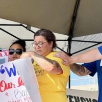 Crystal Londonio, wife of detained Machinist Max Lodonio, speaks at the June 6 rally. Richard Howard, the president of her husband’s Machinists local is at right (in hat) with another local member. Photo: Zack Pattin