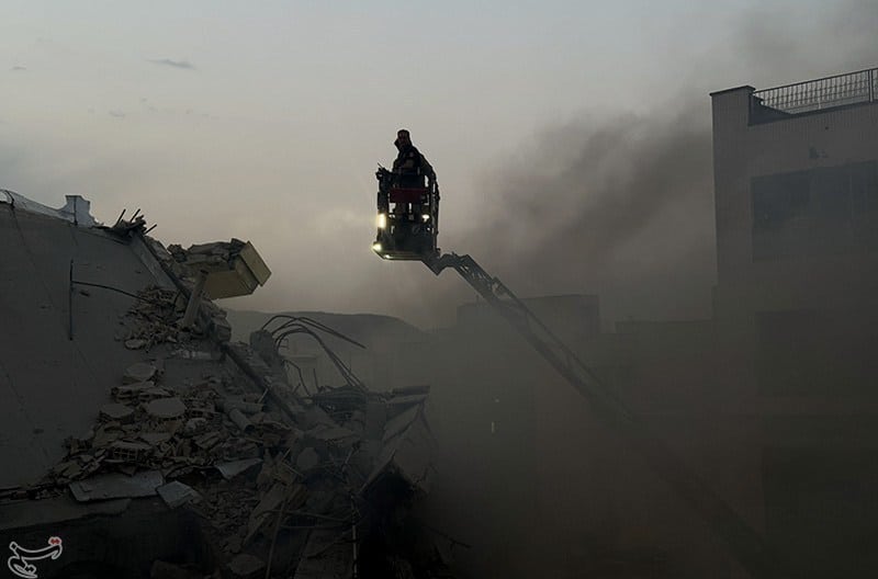  | A person on a crane surveys the ruins of a bombed building surrounded by smoke | MR Online