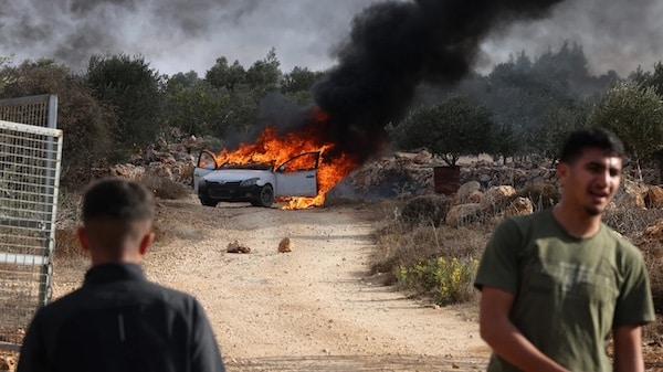 Palestinians stand near a burning car reportedly set alight by Israeli settlers attempting to disrupt them harvesting olives near the occupied West Bank village of Turmus Ayya, on 19 October 2025 (Hazen Badar/AFP)