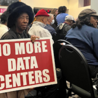 In the back of a crowded town hall meeting on December 10, 2025 Dekalb County resident Sandra Holmes made her opposition to data centers clear with a sign. Credit: Amanda Andrews / GPB News