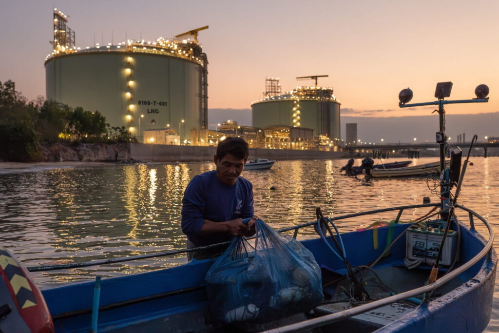 A fisher offloads gear in front of a liquefied natural gas (LNG) terminal operated by state-owned energy company PTT Public Company Limited at the Map Ta Phut Industrial Port in Rayong province, Thailand in February 2026. Photo by Andy Ball for Mongabay.