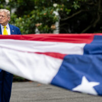 Part of a US flag in the foreground, with President Donald Trump standing in the background.