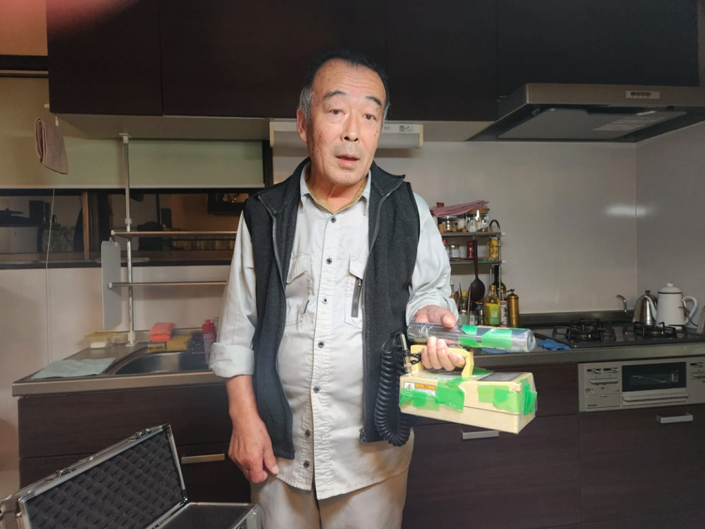 Yukio Shirahige worked for 36 years as a cleaner at Fukushima Daiichi, decontaminating nuclear reactors. Holding a radiation detector, he shows how his house, 15 years after the disaster, is still contaminated. Thomas A. Bass