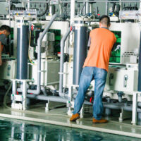 Two men operate large machines on a factory floor.