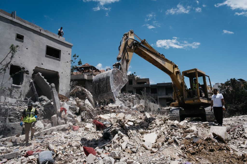 Ahmed Hariri (left) stands near an excavator on May 20, 2026 amid recovery efforts following an Israeli airstrike in Deir Qanoun Al-Nahr. Hairri was killed in an Israeli airstrike on May 22, 2026. Photo by Katrine Dige Houmøller.