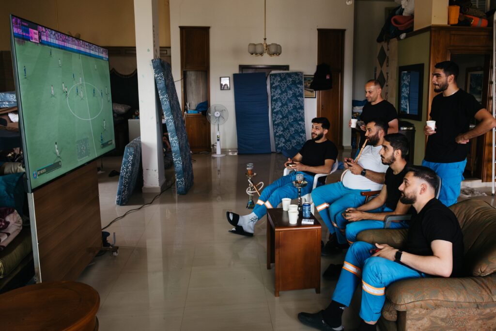 Rescue workers from the Nabatieh ambulance association play FIFA on a PlayStation, ready to go on duty in case of Israeli attacks. Many have lived at Najda Hospital since the war escalated on March 2. Nabatieh, Lebanon. May 18, 2026. Photo by Katrine Dige Houmøller.