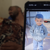 BAHAHA ABU AL-AJEEN AT AL-AQSA MARTYRS HOSPITAL WITH A PHOTO OF HIS SON, RAYYAN. (PHOTO: SCREENSHOT FROM VIDEO TESTIMONY GATHERED BY OSAMA KAHLOUT FOR MONDOWEISS)