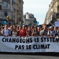 A row of marching protesters hold a long banner that reads, in French, "Change the system, not the climate."