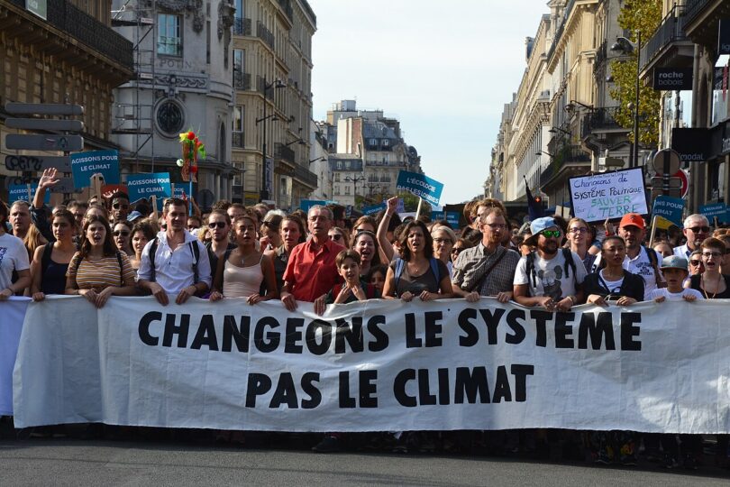 A row of marching protesters hold a long banner that reads, in French, "Change the system, not the climate."