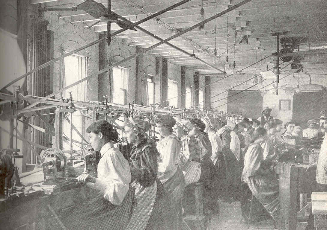 A row of women workers sit at machines used in the manufacture of buttons for clothing.