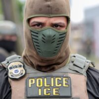 A U.S. Immigration and Customs Enforcement officer watches a crowd of protesters at Delaney Hall, a detention center, in Newark, New Jersey, on May 25, 2026. Employing new tactics, ICE arrested more people in July than in any previous month of the Trump administration. (Photo by Ben Ackman/New Jersey Monitor)
