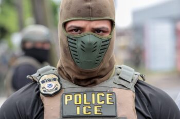 A U.S. Immigration and Customs Enforcement officer watches a crowd of protesters at Delaney Hall, a detention center, in Newark, New Jersey, on May 25, 2026. Employing new tactics, ICE arrested more people in July than in any previous month of the Trump administration. (Photo by Ben Ackman/New Jersey Monitor)