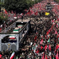 A vast crowd fills a street in Tehran, with many people waving Iranian flags.