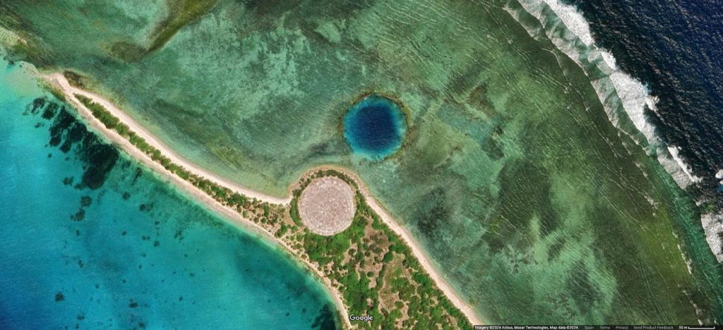 Satellite image of the Runit Dome (in gray), also locally called “The Tomb,” on the Marshall Islands. The dome contains 100,000 cubic yards of radiologically contaminated soil and debris collected from the fallout of the 43 atmospheric nuclear tests conducted at Enewetak Atoll in the Marshall Islands archipelago by the United States between 1946 and 1958. The cleanup operations removed less than one percent of the total estimated radioactive fallout of those tests. The dome, which was completed in 1980, sits on top of the crater created by the “Cactus” 18-kiloton nuclear test of May 6, 1958. The 404-feet-wide crater formed by the “Redwing Lacrosse” 40-kiloton nuclear test of May 5, 1956 is also visible on the image (in blue). (Credit: Airbus / Maxar Technologies, via Google Earth)