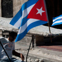 A man sits in a pedicab with two Cuban flags attached to its roof.