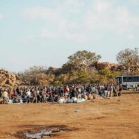 MIGRANT WORKERS GATHER WITH THEIR LUGGAGE BESIDE BUSES AT AN OUTDOOR DEPARTURE AND TRANSIT POINT, AWAITING ONWARD TRANSPORT IN LIMPOPO, SOUTH AFRICA (COPYRIGHT WECARE FOUNDATION, 2026)