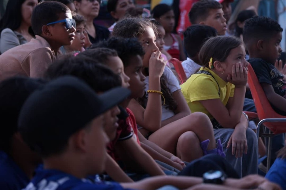 Children sit in the audience at a play, watching intently.