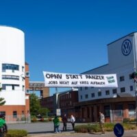 Activists hang a banner on Volkswagen’s Osnabrück plant in May 2025 opposing plans to turn the factory toward military production. The banner reads, “Public transit instead of tanks — don’t build jobs on war.”