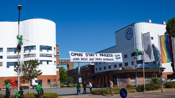 Activists hang a banner on Volkswagen’s Osnabrück plant in May 2025 opposing plans to turn the factory toward military production. The banner reads, “Public transit instead of tanks — don’t build jobs on war.”