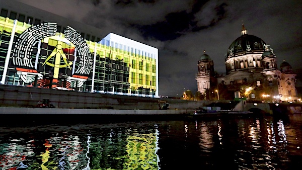 The emblem of the German Democratic Republic is projected onto the front of the ‘Humboldt Forum’ building in Berlin, Nov. 4, 2019. The ‘Humboldt Forum’ was built on the site of the form ‘Palast der Republik’ (Palace of the Republic), where the GDR parliament met. It was demolished by German authorities following the annexation of the GDR. The building on the right is the Berlin Cathedral. | Michael Sohn / AP