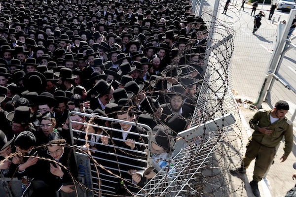 An Israeli soldier stands guard as young men gathered during a demonstration by Ultra-Orthodox Jews against Israel's military draft on June 17, 2026 outside the Beit Lid military base in Kfar Yona, Israel. Photo by Amir Levy/Getty Images.