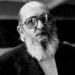A black and white photograph of Paulo Freire later in life. Freire is bald, bearded, and wears large eyeglasses.
